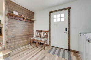 Ett rum med träpanel på väggarna, en vit dörr, två trästolar, ett litet bord och en tvättmaskin.
