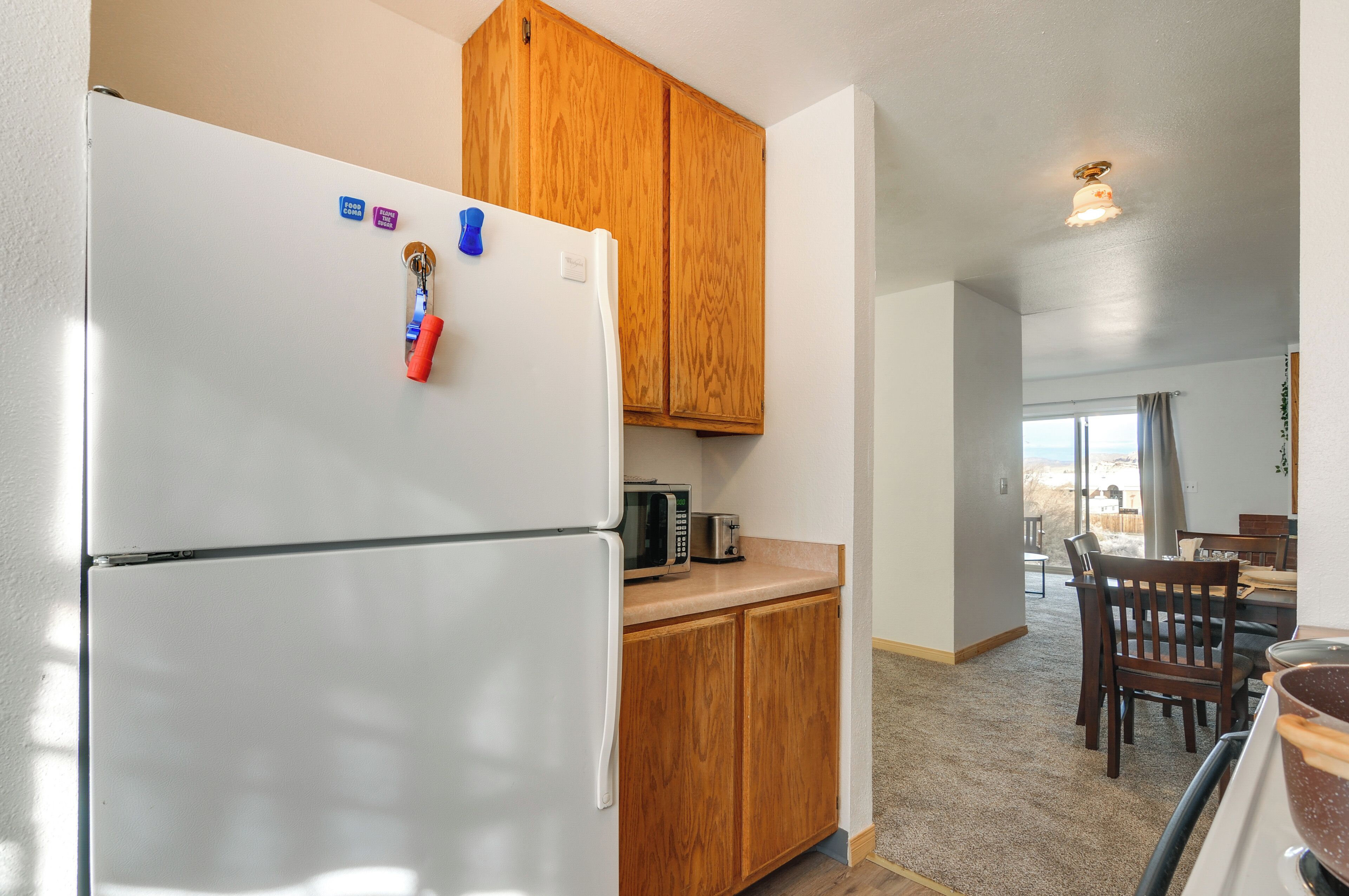 A kitchen with a white refrigerator, wooden cabinets, a microwave, and a dining area with a table and chairs.