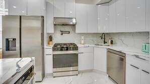 A modern kitchen with white cabinets, stainless steel appliances, and a marble countertop. - 6 Mi to Times Square: Stylish Jersey City Retreat (Jersey City)