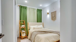 A bedroom with a bed, a wooden ladder, a green curtain, and a macrame wall hanging. - 6 Mi to Times Square: Stylish Jersey City Retreat (Jersey City)