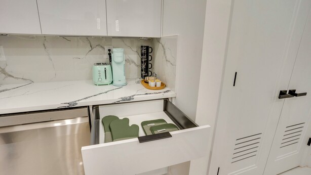 A kitchen with white cabinets, a marble backsplash, and a countertop with a coffee maker, toaster, and a small basket. - 6 Mi to Times Square: Stylish Jersey City Retreat (Jersey City)