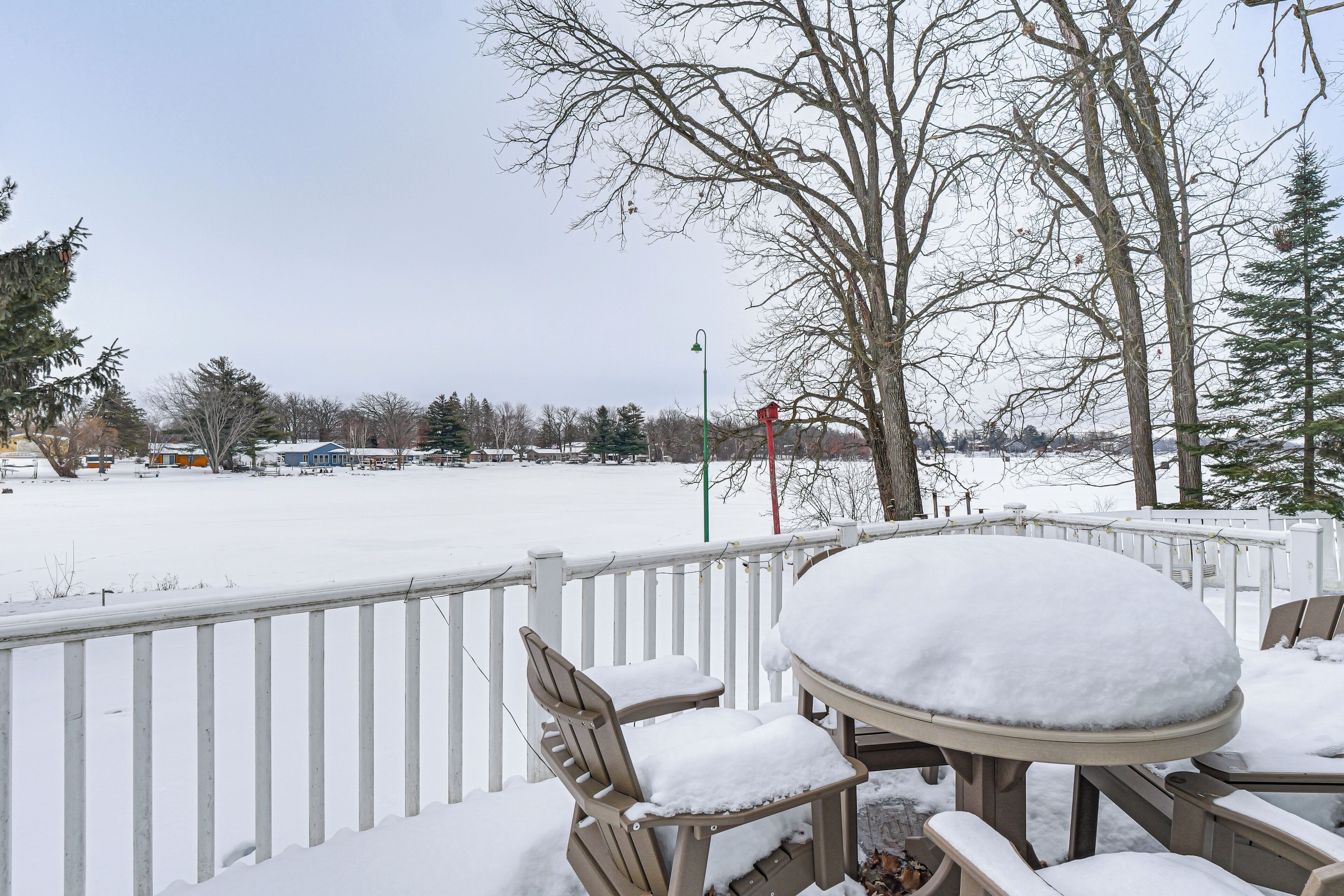 A snow-covered deck with outdoor seating, a view of a snowy landscape, and leafless trees.