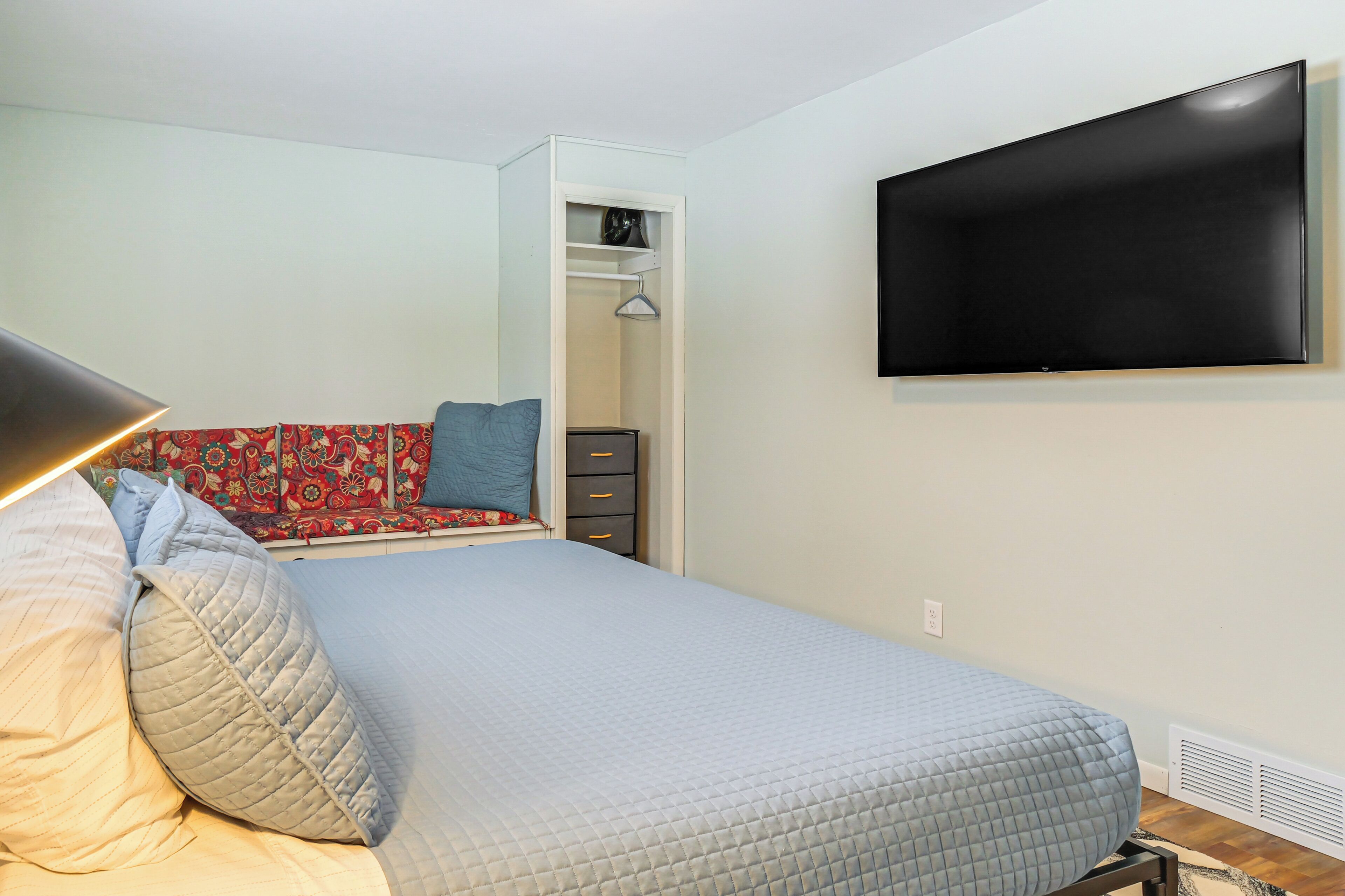 A bedroom with a bed, a TV mounted on the wall, a wardrobe, and a bedside table.