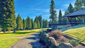 A pathway leading to a modern building with a glass facade, surrounded by a well-maintained lawn and tall trees. - Golf & Hike! Home in Lake Almanor West Community (Chester)