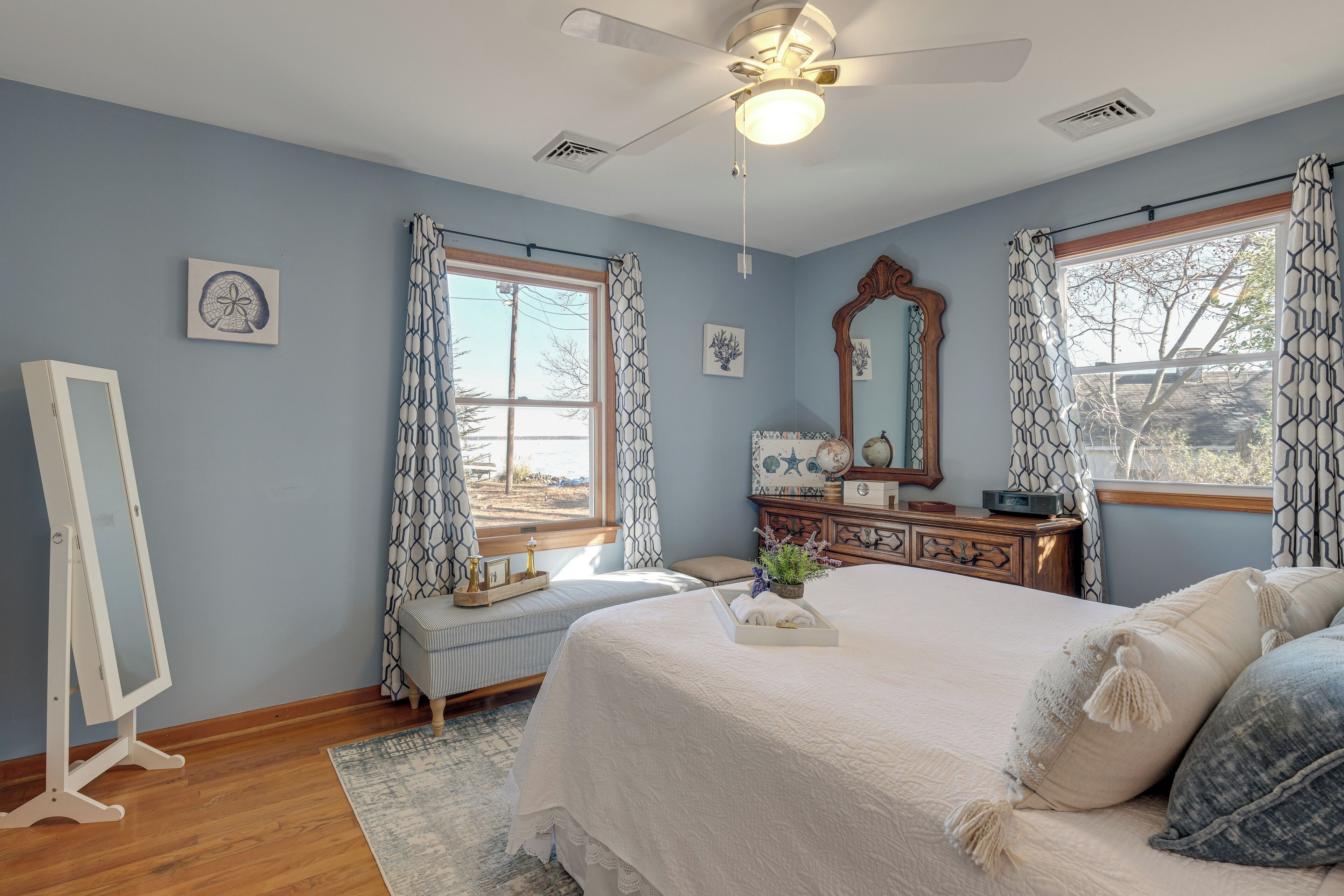 Une chambre à coucher avec un grand lit, un grand miroir, une commode et une fenêtre ornée de rideaux à motifs.