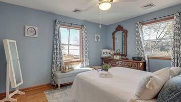 Une chambre à coucher avec un grand lit, un grand miroir, une commode et une fenêtre ornée de rideaux à motifs.