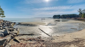 Une plage avec une jetée en bois qui s’avance dans des eaux calmes, entourée d’arbres et de rochers.