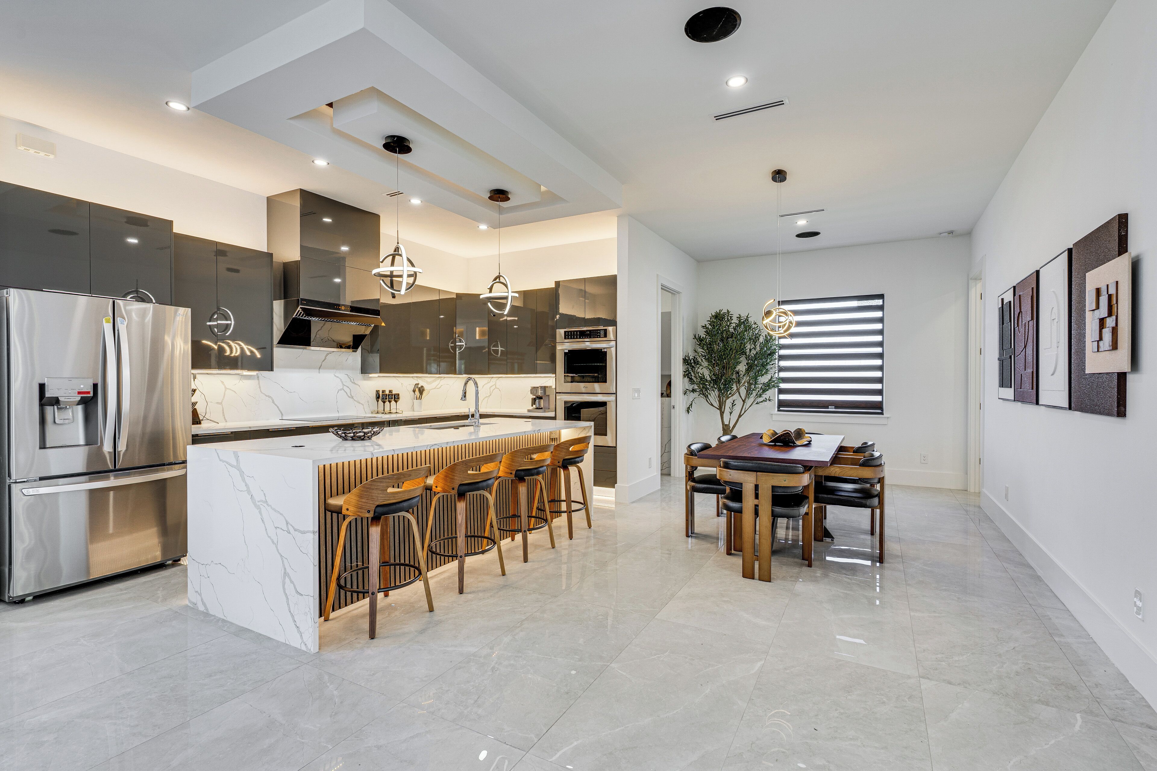 A modern kitchen with a central island, bar stools, a dining table, and a refrigerator.