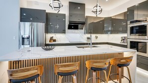 A modern kitchen with a large island, stainless steel appliances, and wooden bar stools. - Luxe Outdoor Space! Pet-friendly Cape Coral Home (Cape Coral)