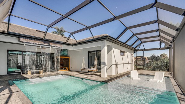 A modern outdoor swimming pool with a glass ceiling, clear water, and lounge chairs. - Luxe Outdoor Space! Pet-friendly Cape Coral Home (Cape Coral)