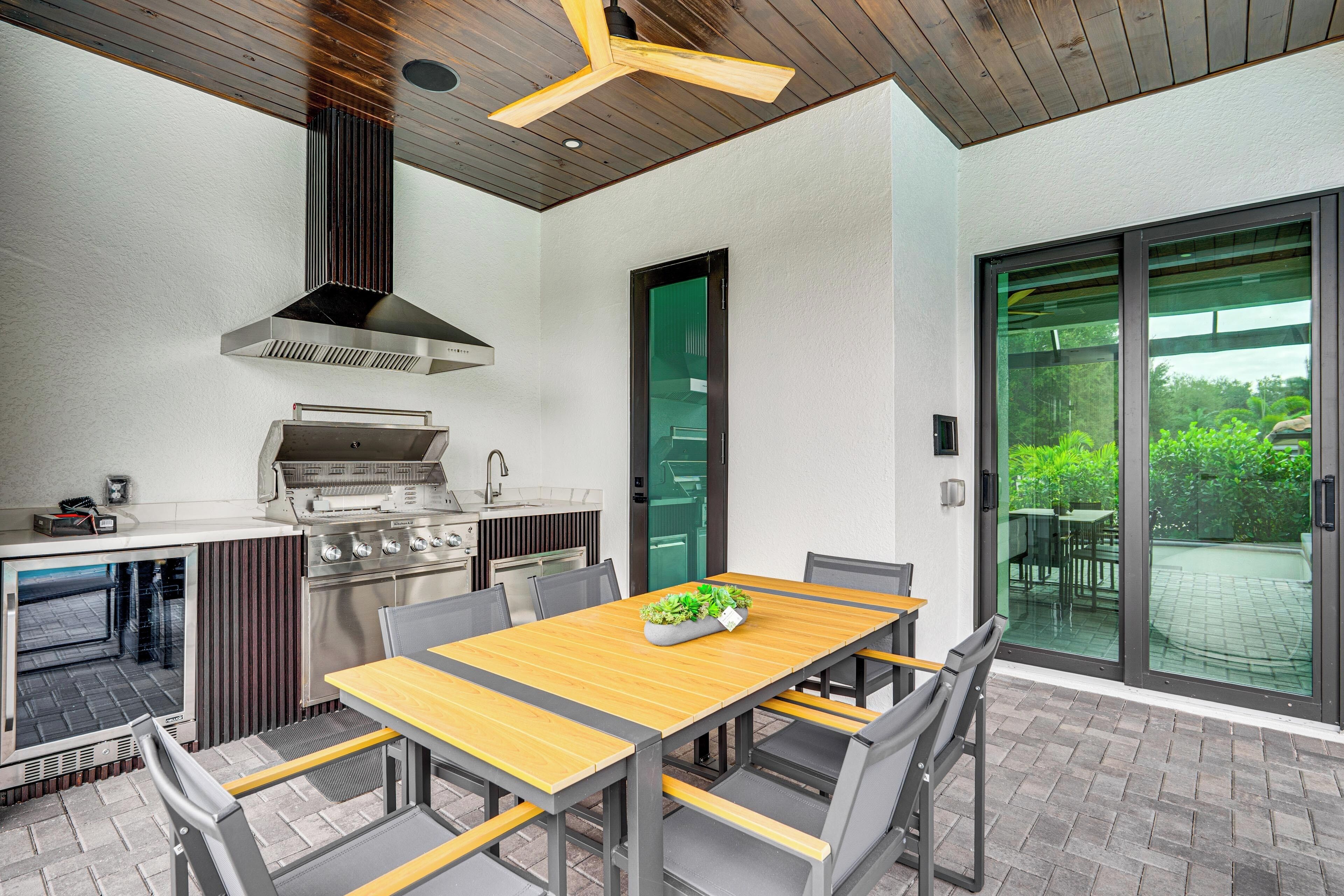 An outdoor kitchen with a wooden table, chairs, and a grill.