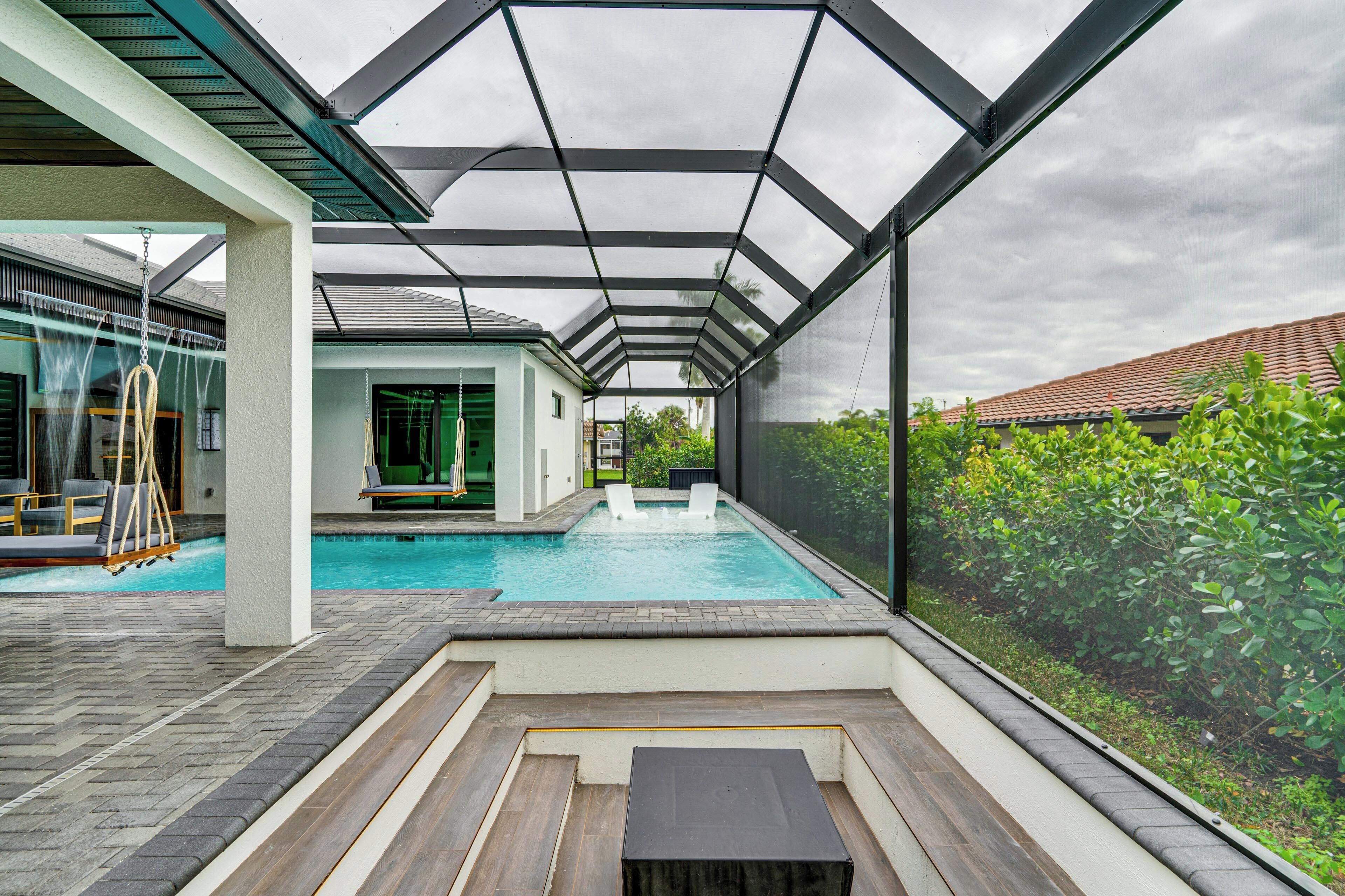 Ein moderner Poolbereich im Freien mit Glasverkleidung, einer Holzterrasse und Blick auf ein Wohngebäude.