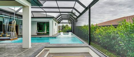 Ein moderner Poolbereich im Freien mit Glasverkleidung, einer Holzterrasse und Blick auf ein Wohngebäude.