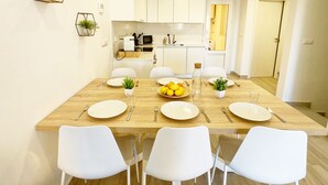 A modern dining area with a wooden table set for four, white chairs, and a kitchen in the background. - Spacious 3-bedroom semi-detached house in kilometer 14 (La Manga del Mar Menor)