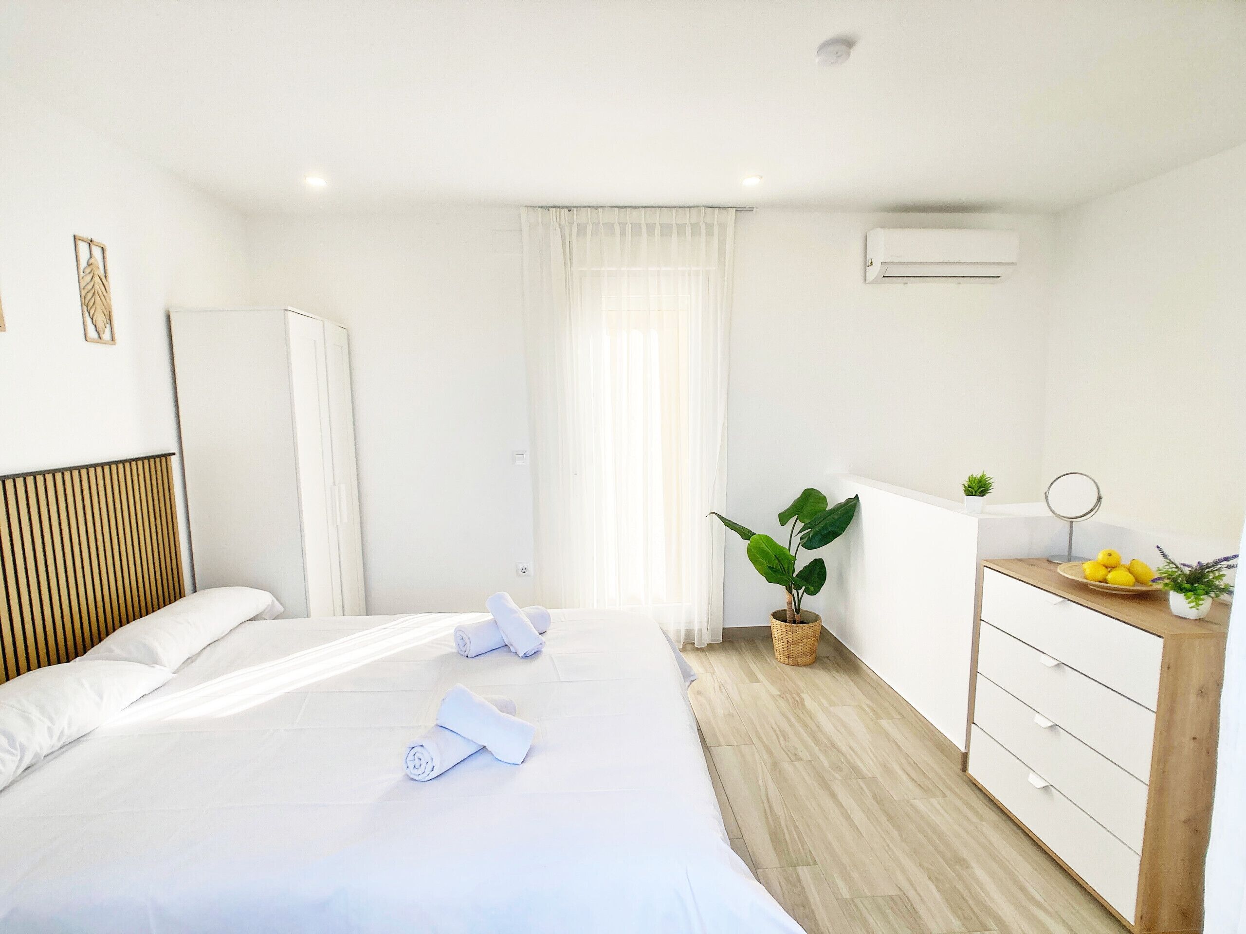 A hotel room with a bed, a dresser, a potted plant, and a small table with lemons and a plant.
