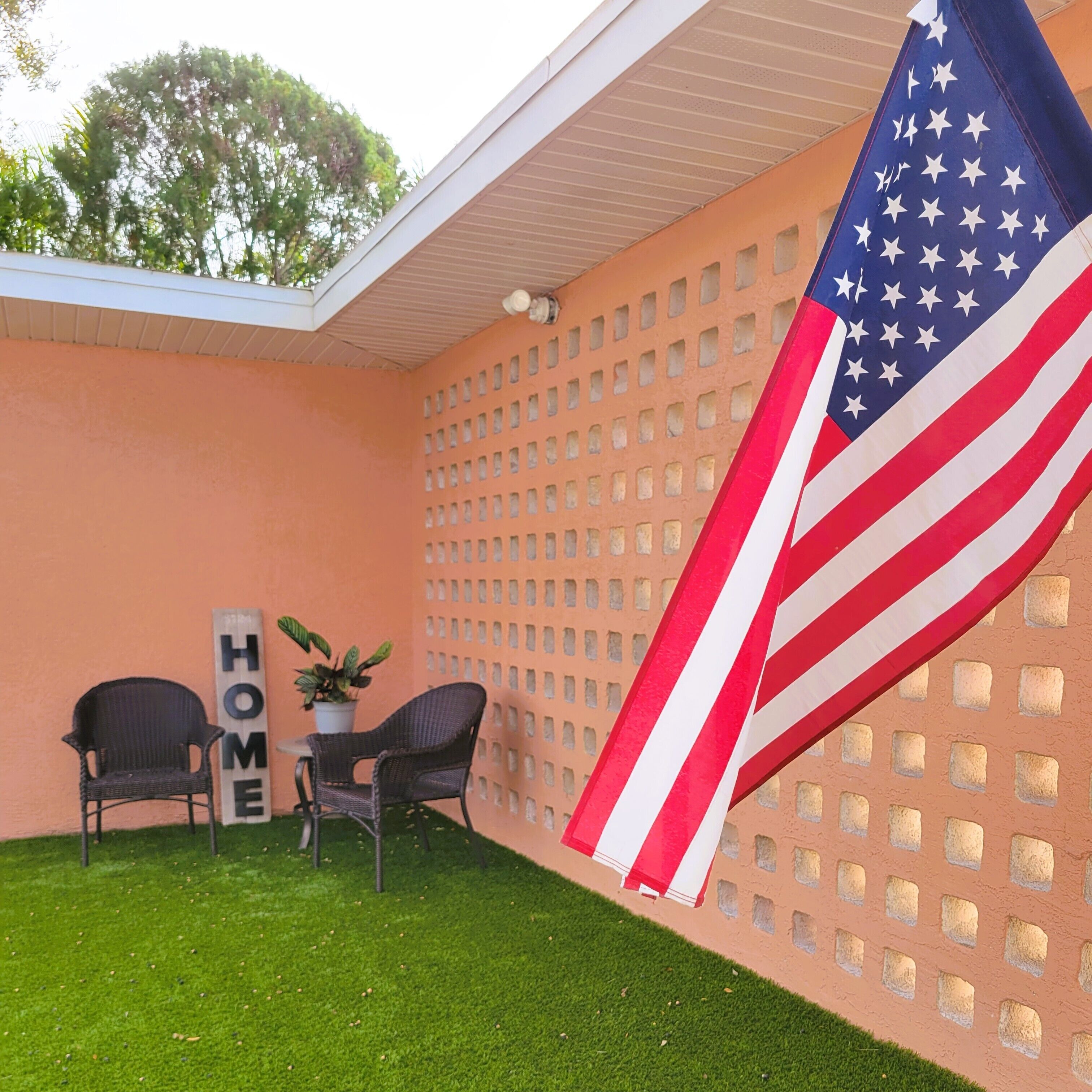 A patio with two wicker chairs, a small table, a potted plant, and an American flag.