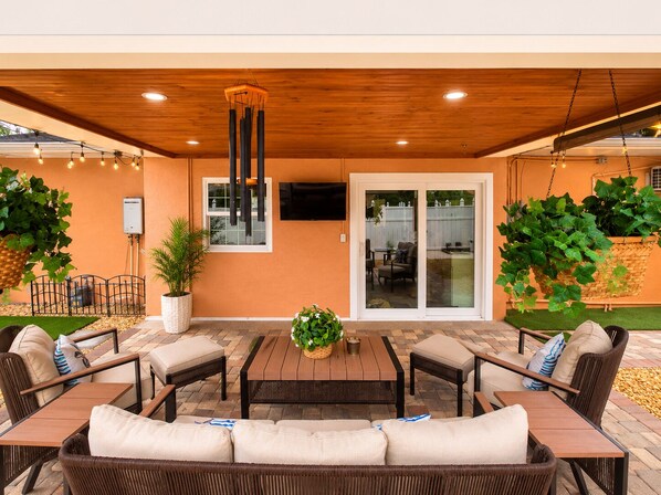 Une terrasse extérieure dotée d’un plafond en bois, d’une table centrale, ainsi que de chaises et de canapés disposés tout autour.