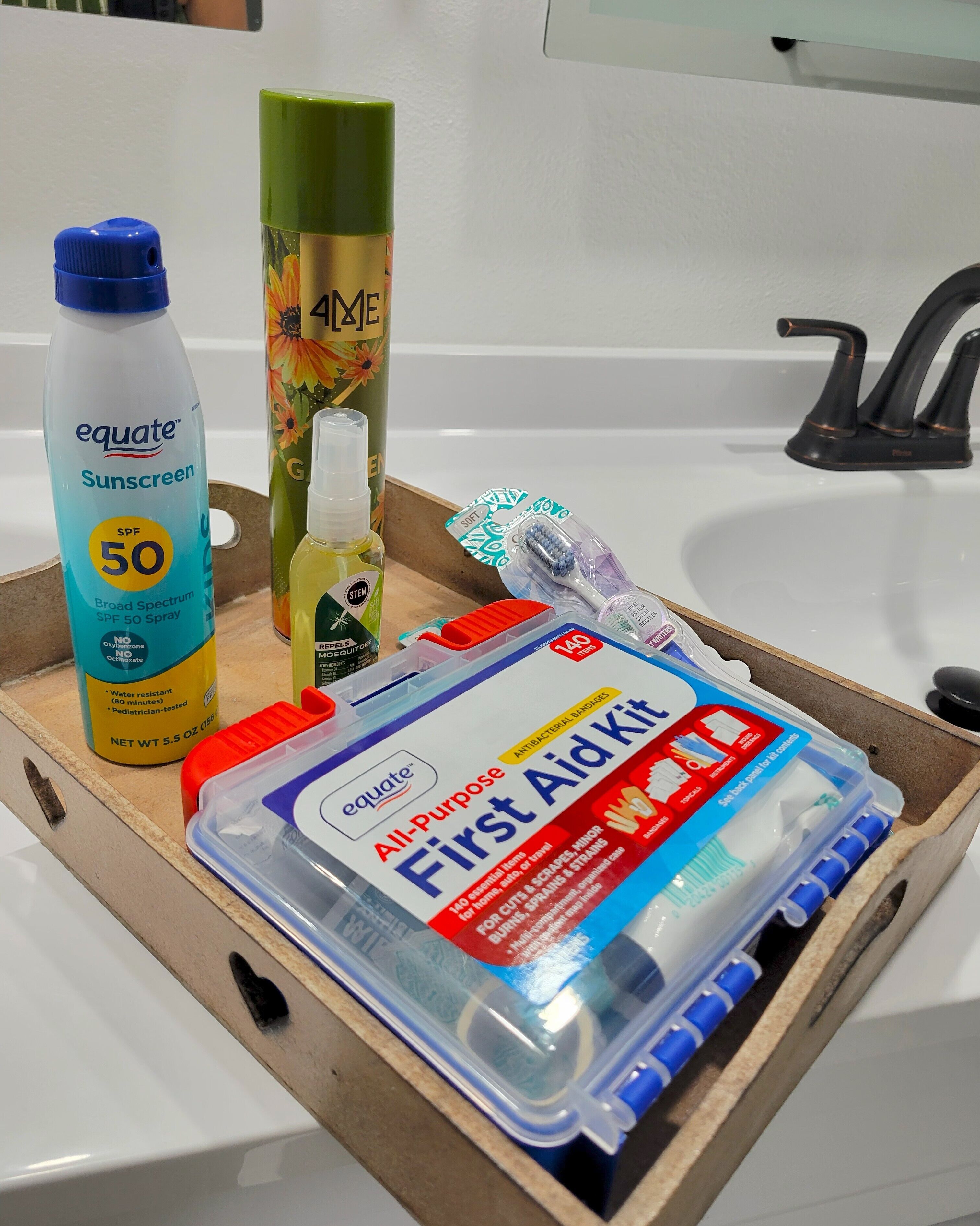 Een houten dienblad met een fles Equate zonnebrandfactor 50, een tube aloë vera gel, een pakje flosdraad en een EHBO-kit.