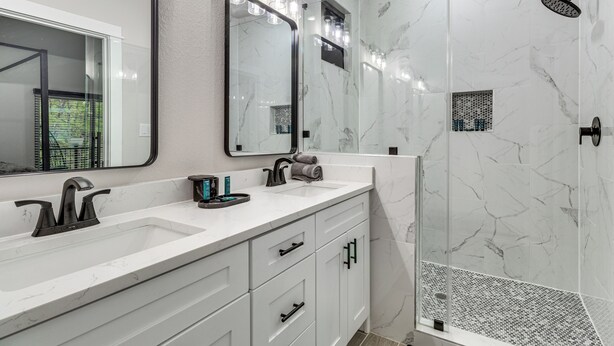 A modern bathroom with a large mirror, a sink with a black faucet, and a shower area with a glass door. - Treehouse Escape in Tahitian Village (Bastrop)