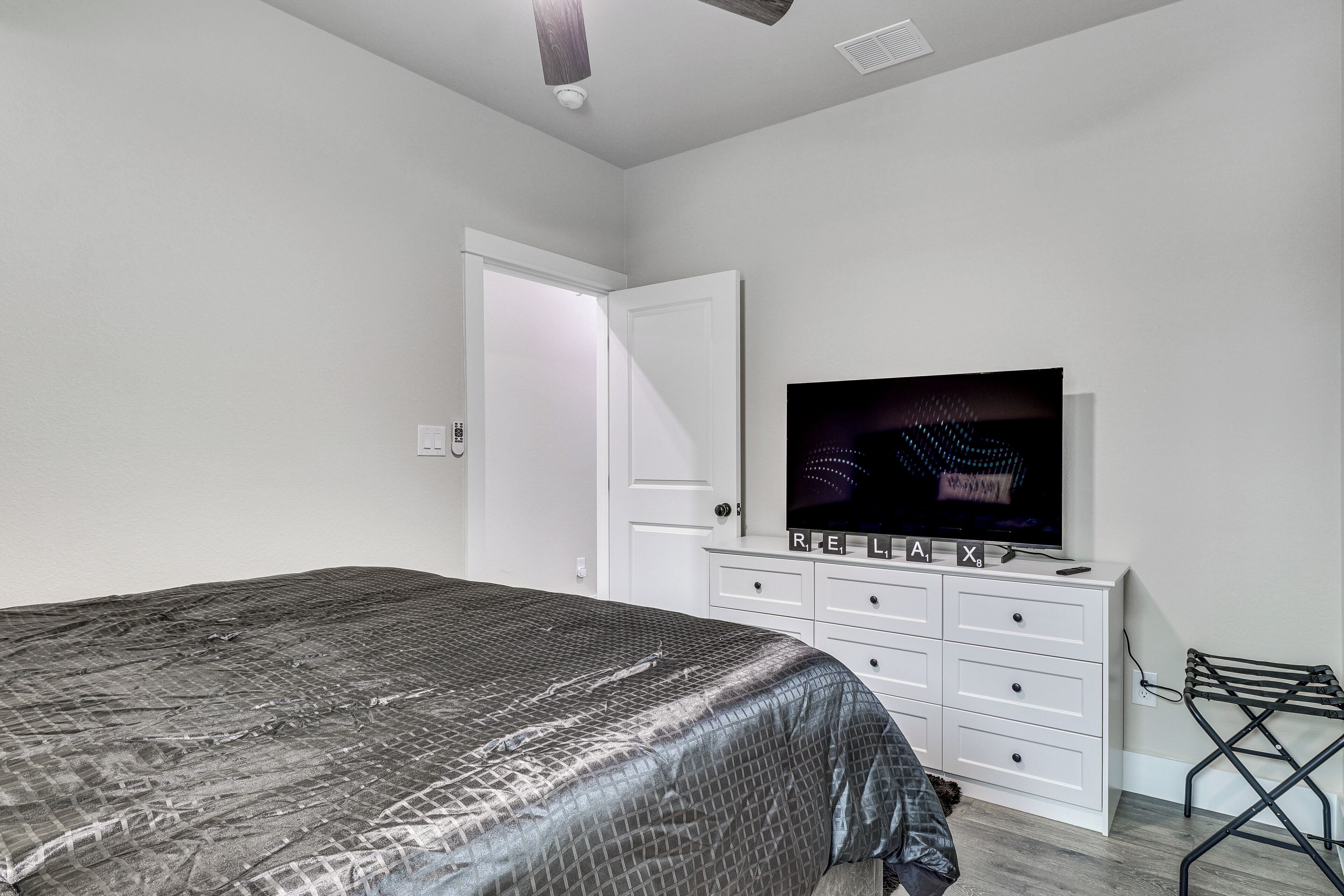 A bedroom with a bed, a TV on a dresser, a door, and a laundry rack.