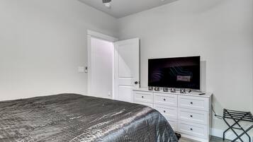 A bedroom with a bed, a TV on a dresser, a door, and a laundry rack.