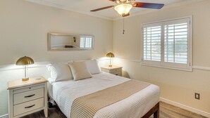 A bedroom with a bed, nightstands, a ceiling fan, a window with blinds, a mirror, and a wall outlet. - Cute Home w/ Boat Parking, Monthly Specials (Lake Havasu City)