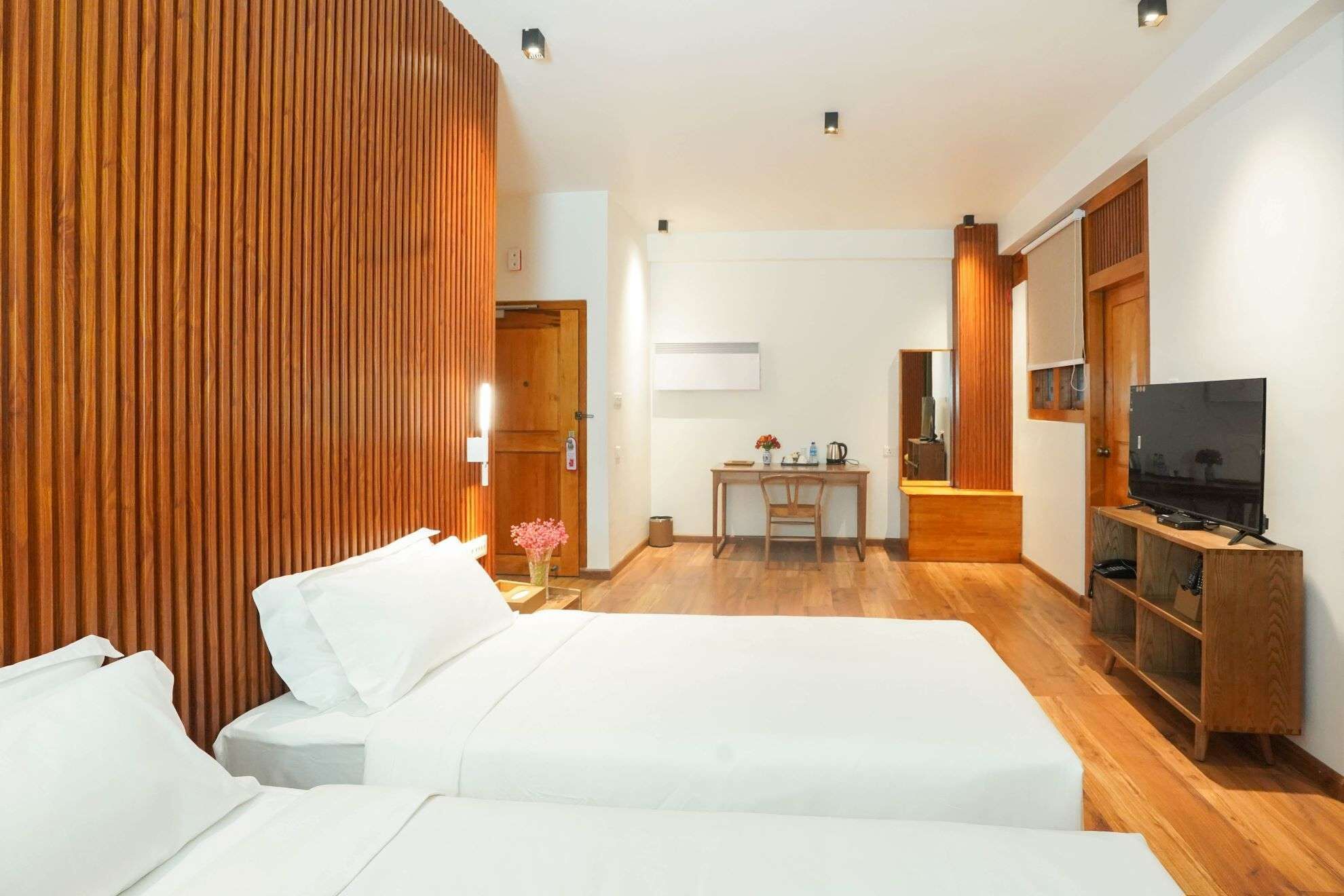 Ein Hotelzimmer mit zwei Betten, einem Schreibtisch mit Stuhl, einem Fernseher und Holzvertäfelung.