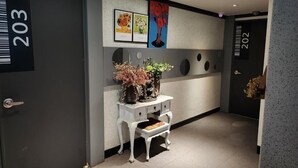 A hallway with a white console table, a vase of flowers, and a wall-mounted artwork. - Alps motel (Incheon)