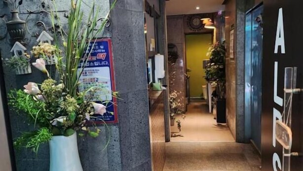 A hotel reception area with a large white vase of flowers, a clock, and a sign for the ALS Motel. - Alps motel (Incheon)