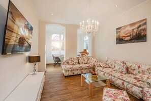 A living room with a sofa, a glass coffee table, a chandelier, and artwork on the walls. - Comfortable vacation apartment Villa Ute Whg. Vanessa only 600 m from the sandy beach Bansin (Bansin)
