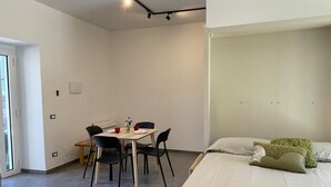 Quarto moderno com cama, mesa de jantar com cadeiras e pequena cozinha.