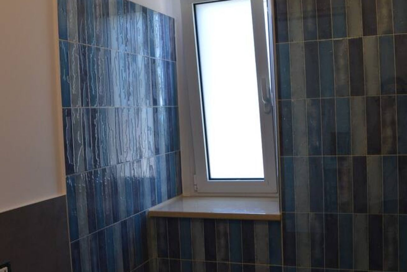A bathroom with blue-tiled walls and a window.