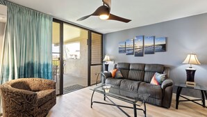 Ein modernes Wohnzimmer mit Sofa, Sessel, Glastisch und Deckenventilator.