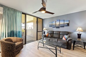 A modern living room with a sofa, armchair, glass coffee table, and a ceiling fan. - Kamaole Sands #10-313 Ocean View, Large Lanai, Walk to the Beach (Kihei)