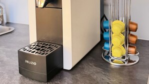 A coffee machine with a drip tray and a metal container holding coffee capsules. - Chalet Achat by Zermatt Premium Apartments (Zermatt)