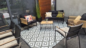 A modern outdoor seating area with a glass wall, a wooden wall, and a patterned rug.