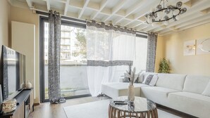A modern living room with a sofa, a coffee table, and a TV. There are patterned curtains and a ceiling light fixture.