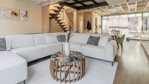 A modern living room with a white sectional sofa, a round coffee table, and a staircase leading to an upper floor.