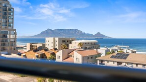 A coastal residential area with modern buildings, a prominent mountain in the background, and a clear blue sky. - Atlantic Terraces 19 (Cape Town)