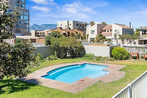 Una piscina rodeada por un césped bien cuidado, con edificios modernos al fondo.