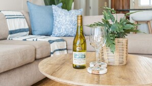 A round wooden table with a bottle of wine, a glass, and a woven basket with a plant. - Atlantic Terraces 19 (Cape Town)