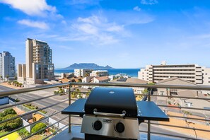 A balcony with a built-in grill overlooking a cityscape and the ocean. - Atlantic Terraces 19 (Cape Town)