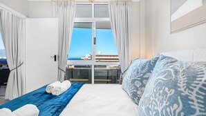 A hotel room with a bed, a massage table, and a view of the city through large windows. - Atlantic Terraces 19 (Cape Town)