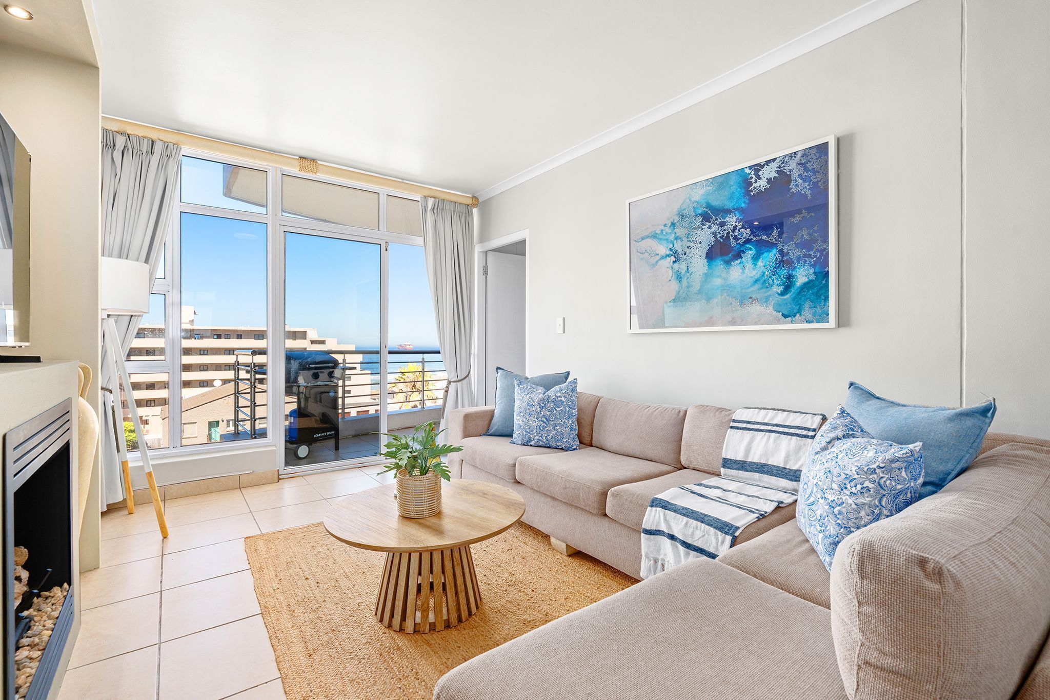 A modern living room with a beige sofa, a round wooden coffee table, and a large abstract painting on the wall.