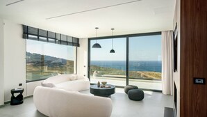 A modern living room with a curved sofa, a round coffee table, and a view of the ocean. - New Luxury Villa w/ Private Pool, Spa & Sea Views! (Heraklion)