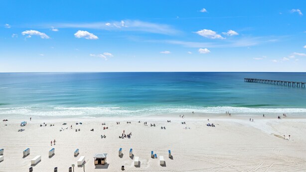 Ein Strand mit einer Seebrücke, die ins Wasser ragt, feinem Sand und Liegestühlen.