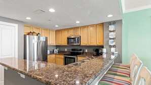 Eine Küche mit Granit Arbeitsplatten, Edelstahlgeräten, Holzschränken und einer Frühstückstheke mit gestreiften Stühlen.