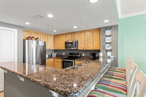 Eine Küche mit Granit Arbeitsplatten, Edelstahlgeräten, Holzschränken und einer Frühstückstheke mit gestreiften Stühlen.