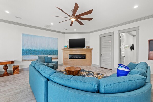 A modern living room with a sectional sofa, a fireplace, a ceiling fan, and a large painting.