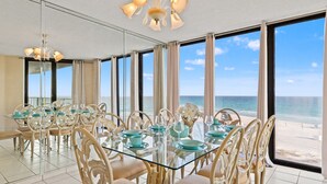 Ein Essbereich mit Glastisch und Stühlen, großen Fenstern mit Blick auf den Strand und einer Deckenleuchte.